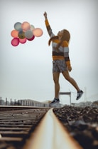 woman holding balloons while jumping on train railways