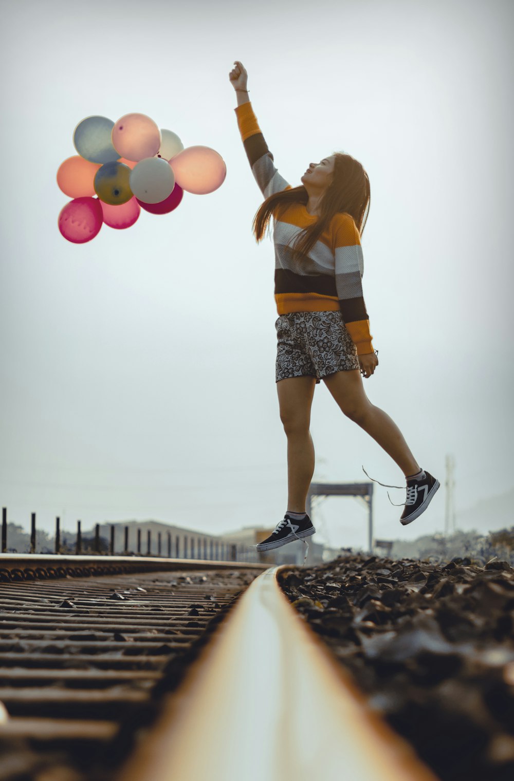 woman holding balloons while jumping on train railways