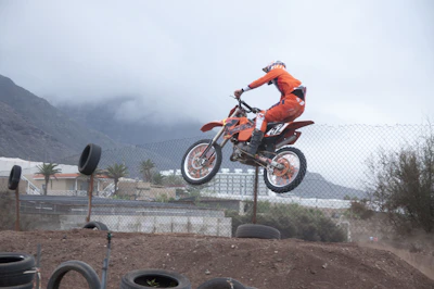 Rider performing a jump on a pitbike with orange accents in a forest setting