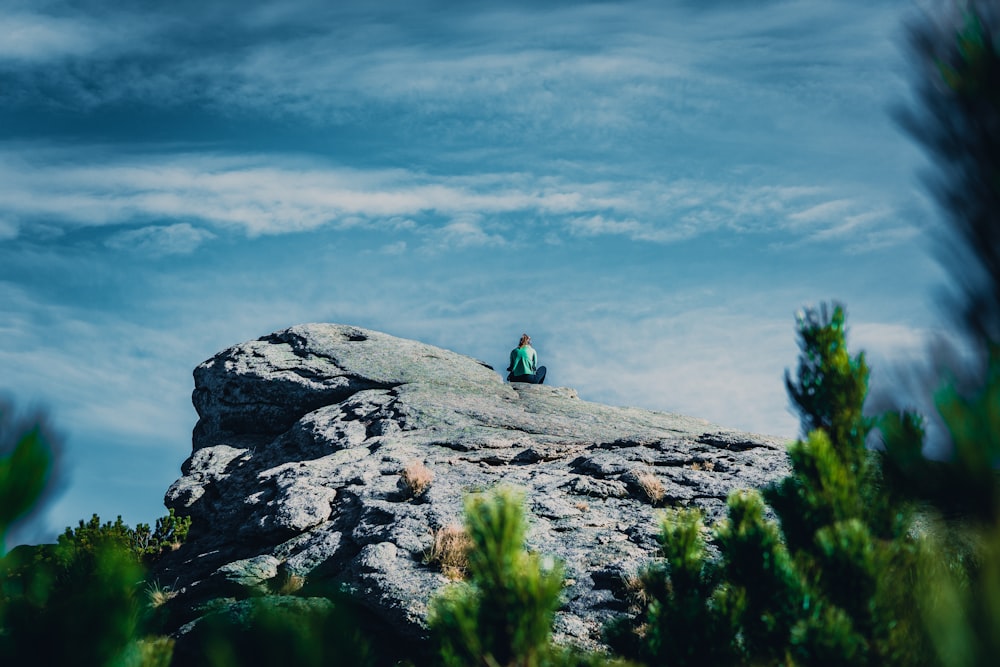 person sitting on cliff under cloudy sky during daytime