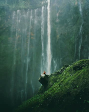 aerial photography of person sitting on rocks near waterfalls