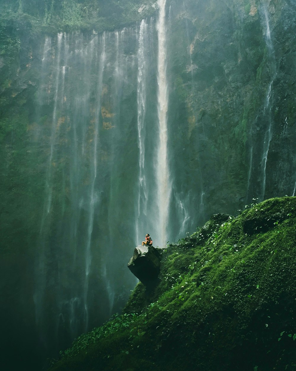 Photographie aérienne d’une personne assise sur des rochers près de chutes d’eau