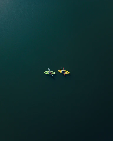 Two friends laughing as they kayak side by side along a peaceful marshland.
