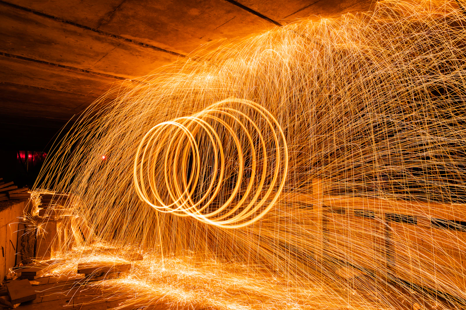 Long-exposure golden spark trails looping and scattering through a dark concrete tunnel