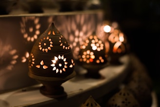 Several ornamental lanterns made of clay emit a warm glow, casting intricate floral patterns of light and shadow onto a nearby surface. The arrangement creates a cozy, intimate atmosphere with a soft focus in the background.