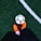 A person is standing on a grass soccer field wearing bright orange soccer shoes next to a black and white soccer ball. The field has a clearly marked white line.