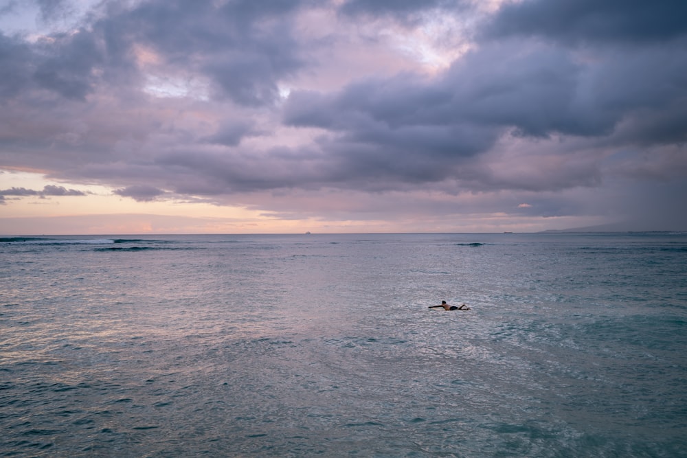 a person riding a surfboard in the ocean under a cloudy sky