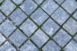 Interlocking stone pavers arranged in a diagonal grid pattern with patches of green moss filling the spaces between the stones.