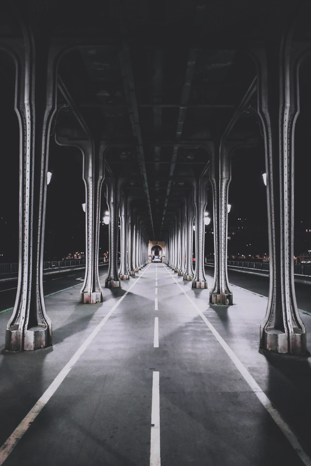 A road under a long colonnade of iron pillars at night, every line running to one vanishing point