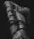 A black-and-white photograph of a nude human body wrapped tightly in dark chains, creating a contrast between the skin and the metal. The focus is on the intertwined limbs and the texture of the chains against the skin.