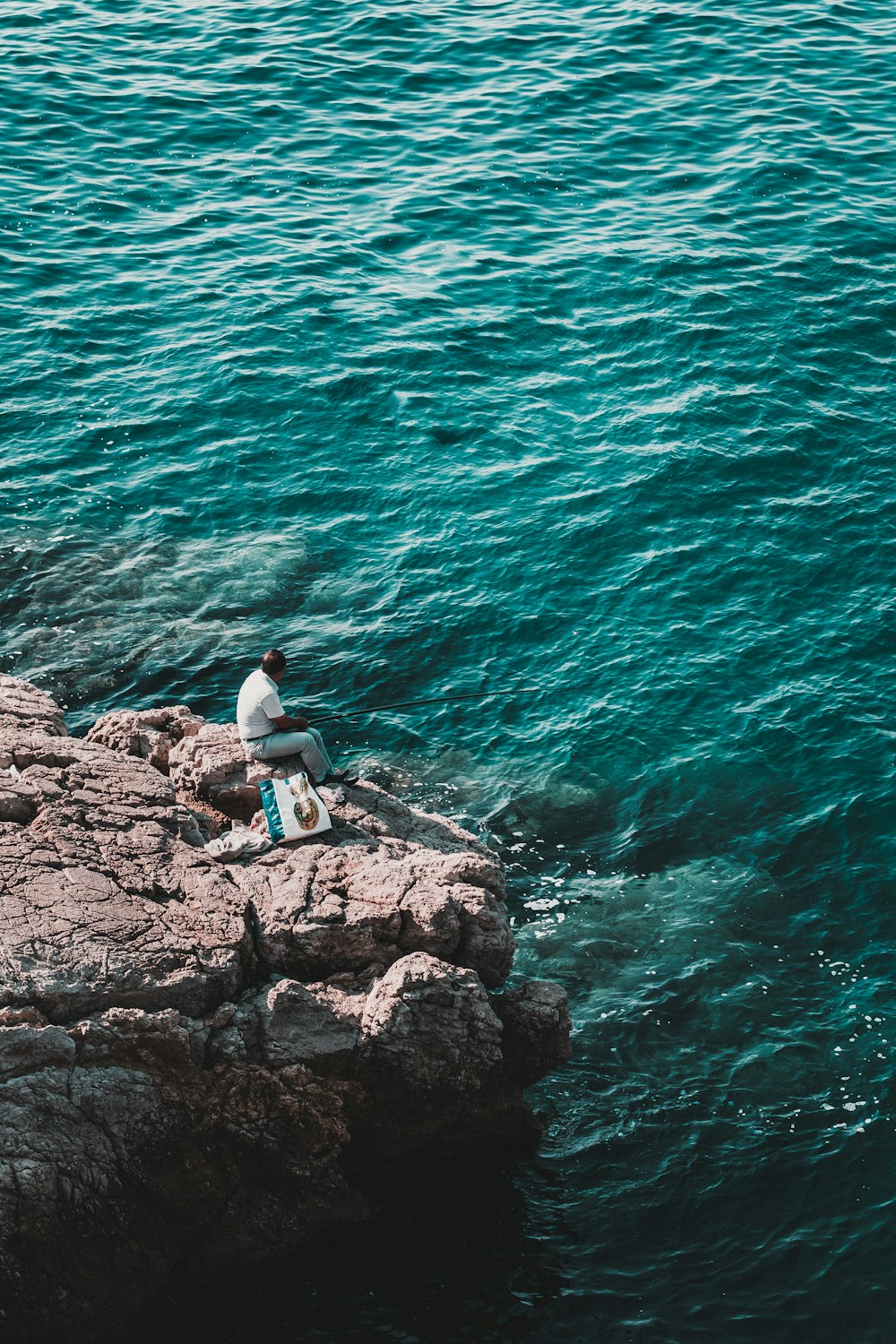 Hombre sentado en la roca cerca del cuerpo de agua durante el día