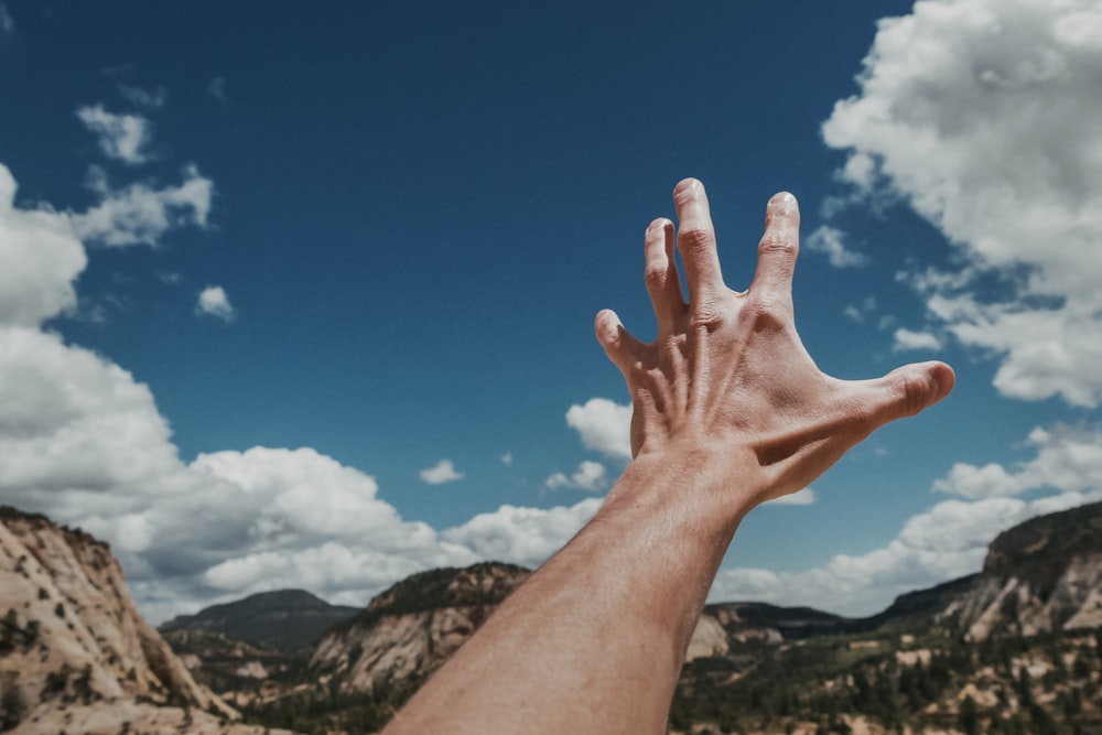 Foto der linken menschlichen Hand, die den Himmel erreicht