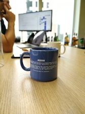 Close-up of blueprints and a coffee cup on a wooden table in a bright office.