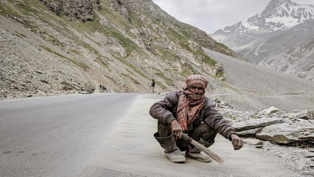 man sitting on gray concrete road holding stick broom