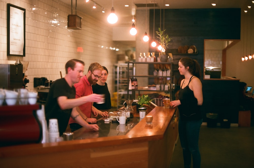 woman in black tank top stands in front of counter with three men inside