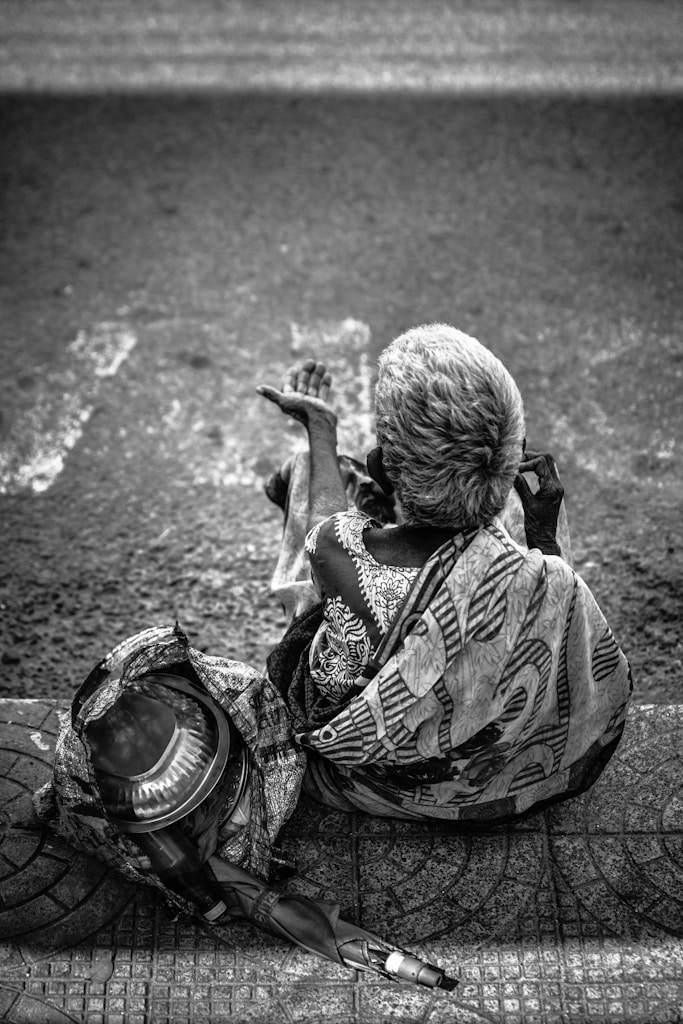 grayscale photography of person sitting near road