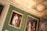 A richly decorated interior wall featuring ornate gold moldings and an elaborate crest. The wall is adorned with several framed paintings. The paintings depict historical figures in period attire. The background features a luxurious green patterned wallpaper.