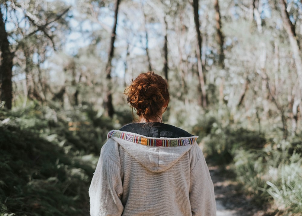 Fotografía de enfoque selectivo de mujer con sudadera con capucha de pie en el suelo rodeada de árboles