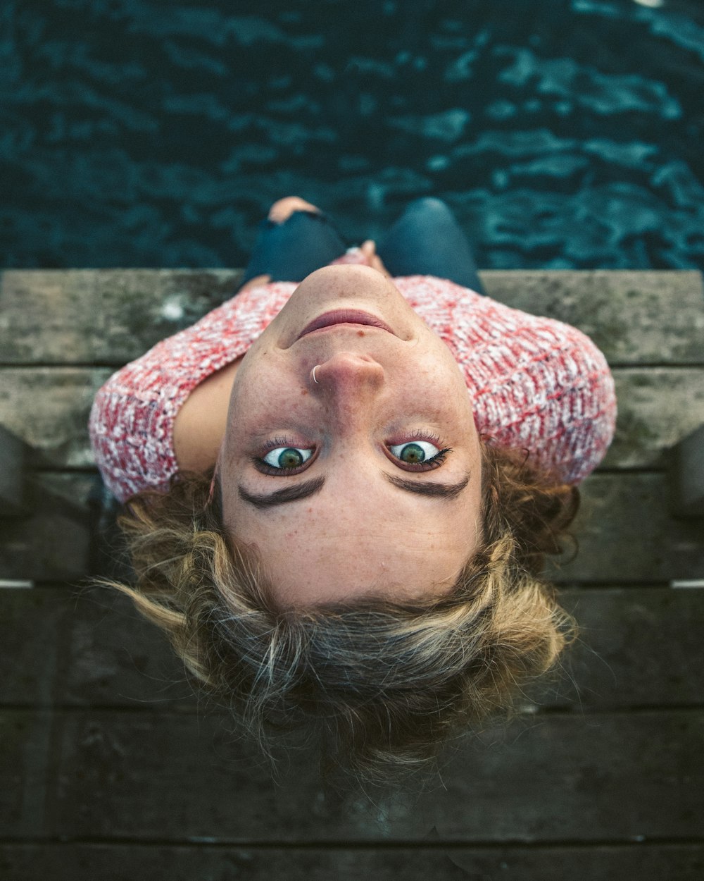 woman looking up while sitting on dock near water