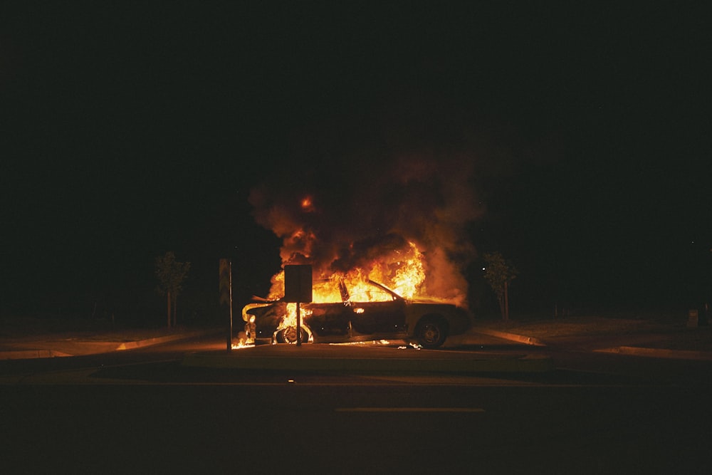 burning grey sedan near trees and signboard at night