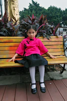 A young girl sitting on a wooden bench, wearing a vibrant, comfortable dress from Vorzaya.