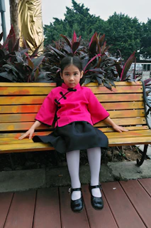 A little girl sitting gracefully on a vintage wooden bench wearing a sharara set with subtle gold accents, surrounded by festive lanterns.