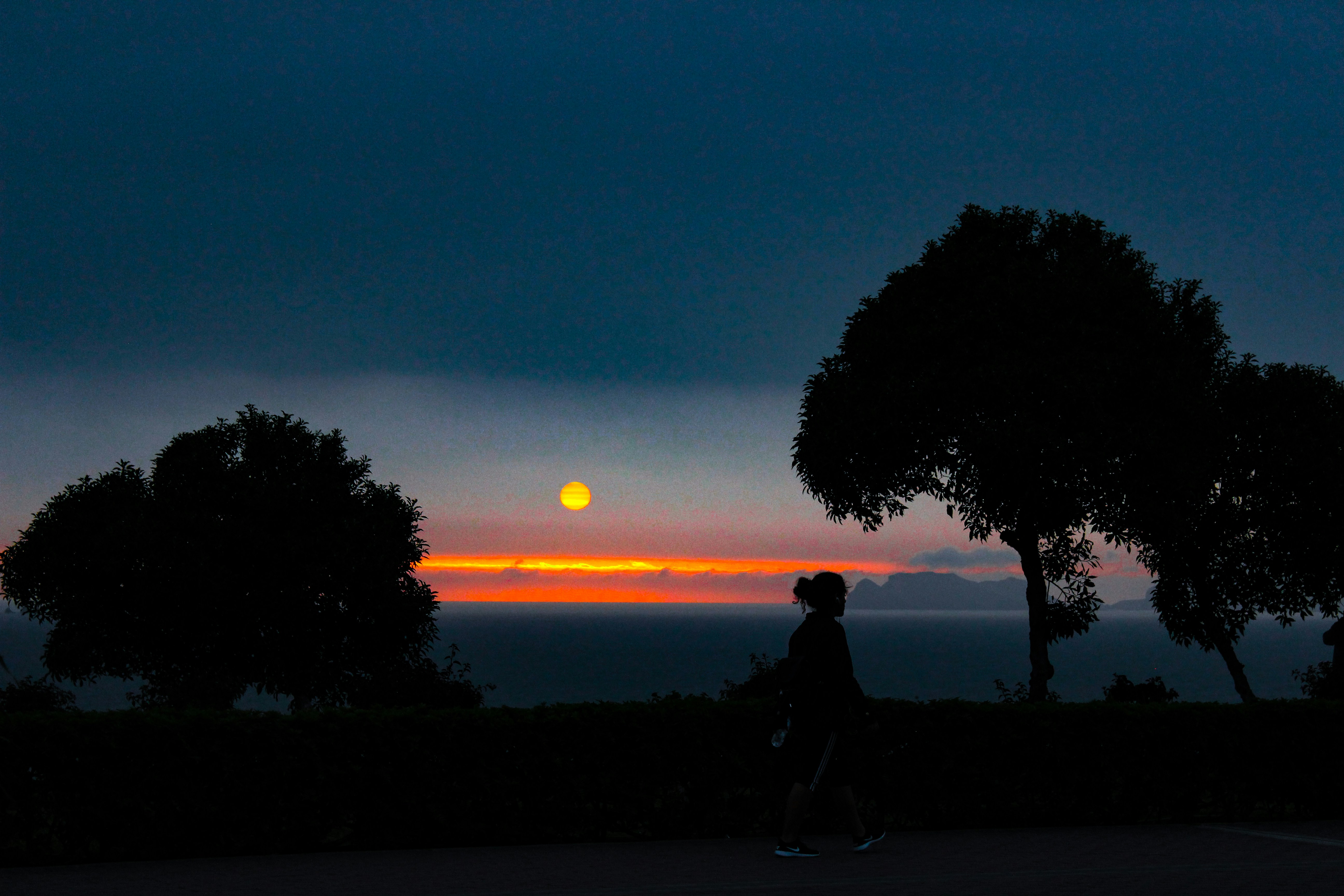 silhouette of woman walking near trees, 5:30  sunset. I use to go every Wednesday to see the cool sunset and in one those Wednesday I could capture this moment.