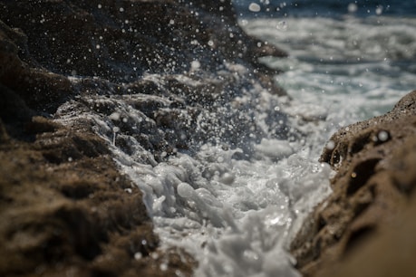 time lapse photography of water making bubbles as it hits the rocls
