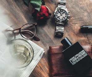 round silver watch, red rose and eyeglasses on wooden surface