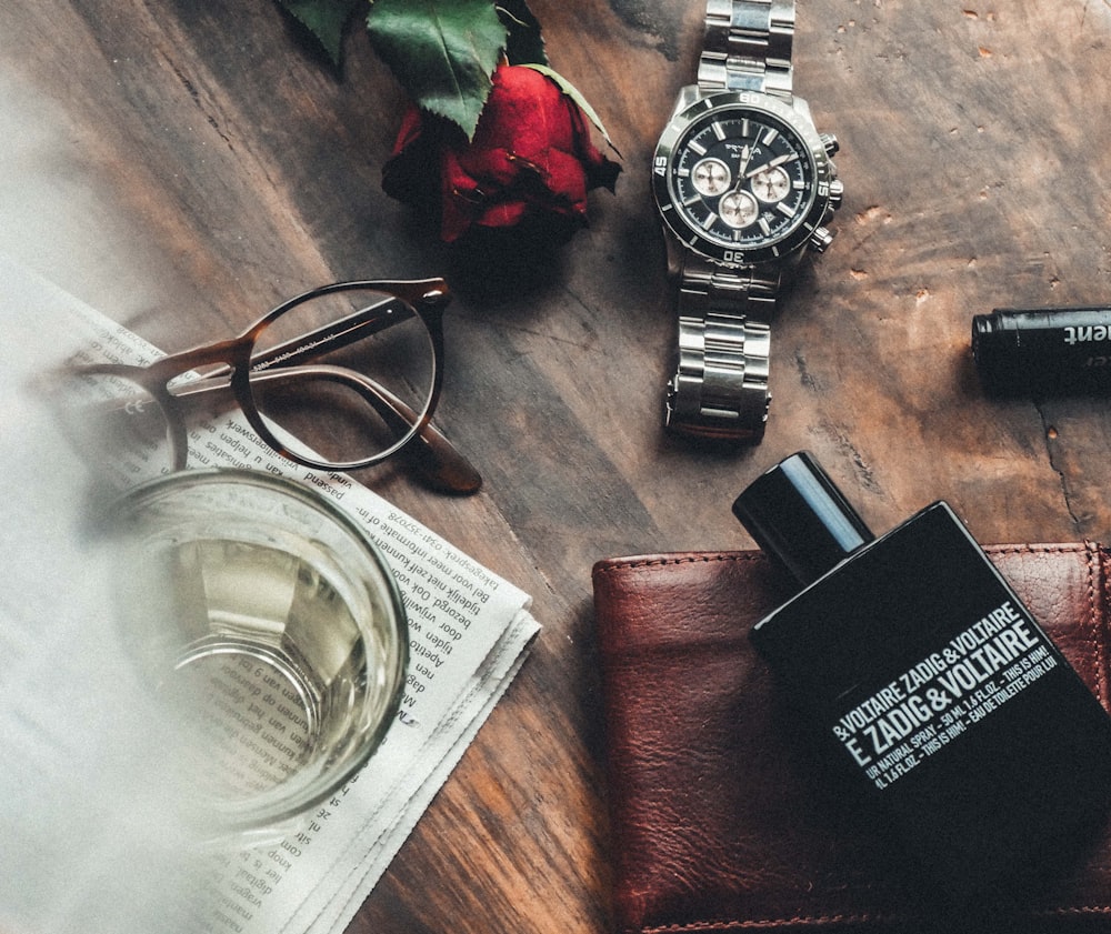 round silver watch, red rose and eyeglasses on wooden surface