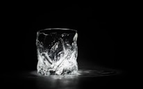 A single, intricately designed glass is placed on a dark surface, illuminated from below. The light enhances the textured surface of the glass, creating intricate patterns and reflections.