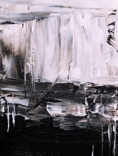 An abstract painting featuring bold brushstrokes in a monochrome palette. The textured canvas displays a mix of light and dark tones, creating a sense of depth and movement. Irregular shapes and lines form a dynamic composition, with a contrast between light grey and dark black areas.