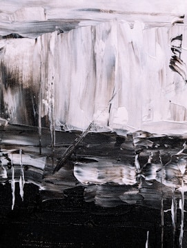 An abstract painting featuring bold brushstrokes in a monochrome palette. The textured canvas displays a mix of light and dark tones, creating a sense of depth and movement. Irregular shapes and lines form a dynamic composition, with a contrast between light grey and dark black areas.