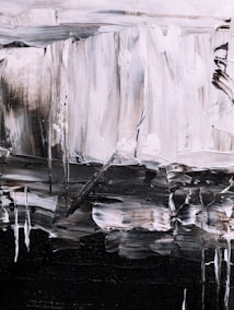 An abstract painting featuring bold brushstrokes in a monochrome palette. The textured canvas displays a mix of light and dark tones, creating a sense of depth and movement. Irregular shapes and lines form a dynamic composition, with a contrast between light grey and dark black areas.