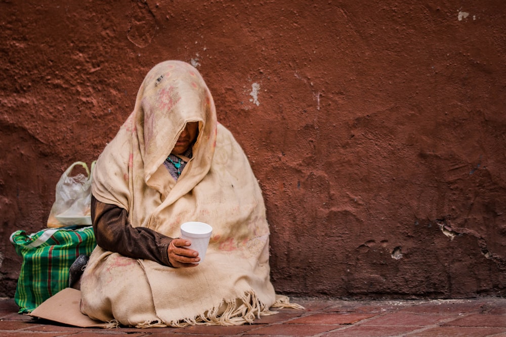 person in scarf holding white disposable cup