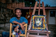 man sitting beside painting on easel