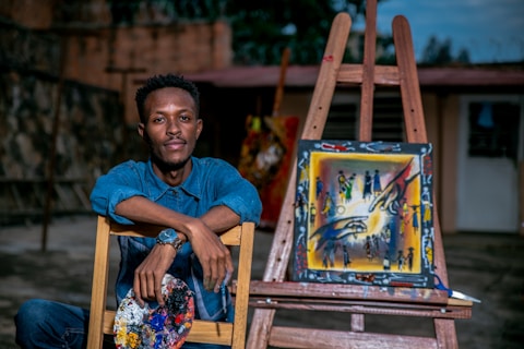 man sitting beside painting on easel