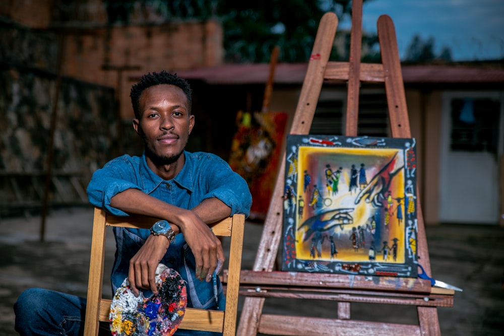 man sitting beside painting on easel