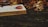 An open book lies on a wooden surface surrounded by colorful autumn leaves. The pages of the book contain musical notes and some text. The scene conveys a sense of tranquility and the onset of fall.