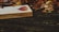 An open book lies on a wooden surface surrounded by colorful autumn leaves. The pages of the book contain musical notes and some text. The scene conveys a sense of tranquility and the onset of fall.