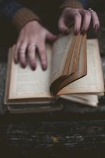 Close-up of hands browsing a novel with colorful covers on a wooden table.