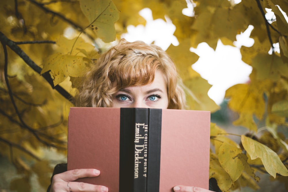 selektive Fokusfotografie einer Frau, die ein Buch von Emily Dickinson hält