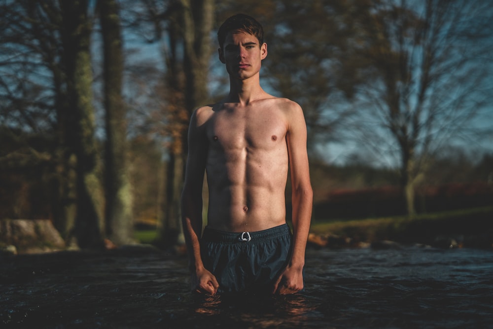 topless man wearing black shorts standing on calm body of water