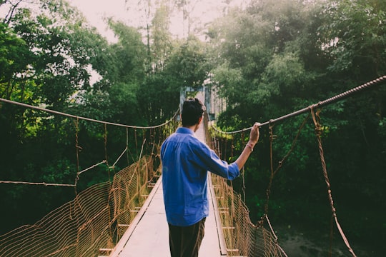 man standing on yellow and brown hanging bridge in Assam India