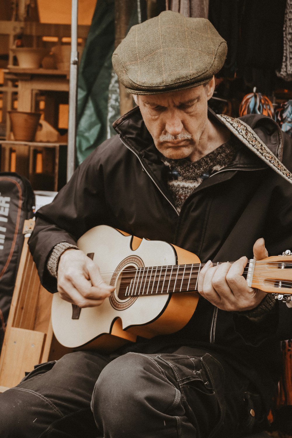 man wearing black jacket playing brown guitar