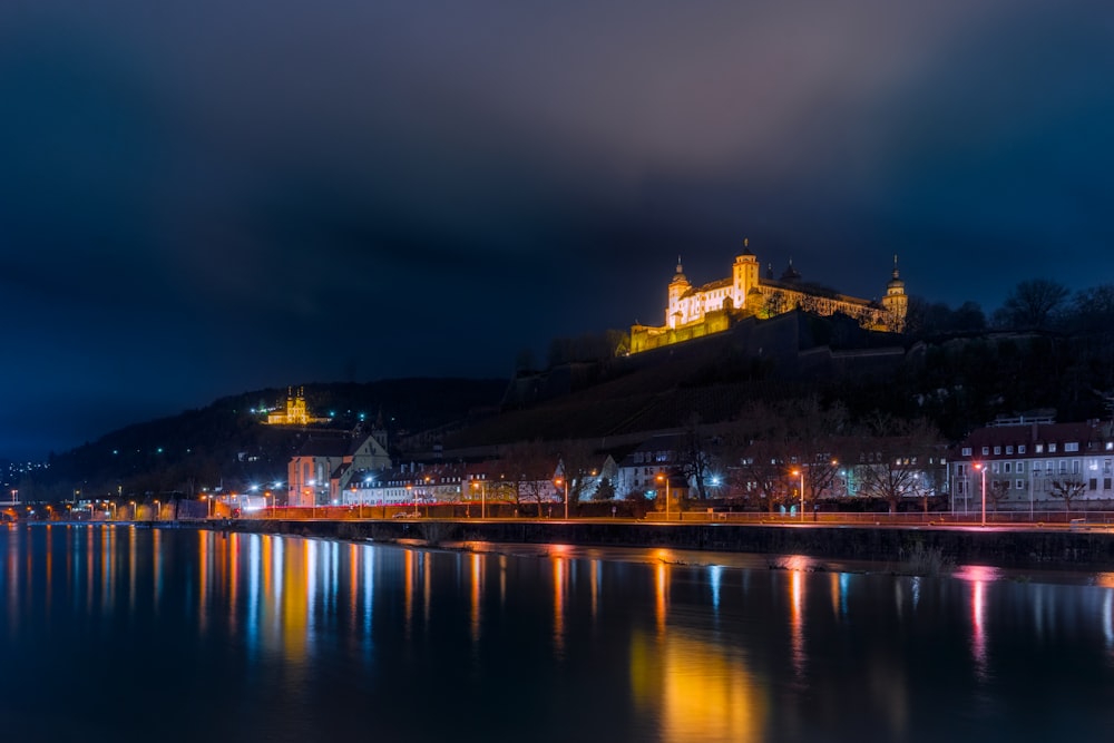 a castle is lit up on a hill above a body of water