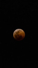 A dark, shadowed moon with a reddish tint is set against a black night sky.