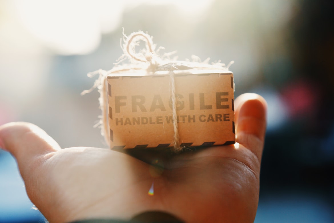Osoba trzymająca na dłoni małą paczkę z naklejką „Fragile”