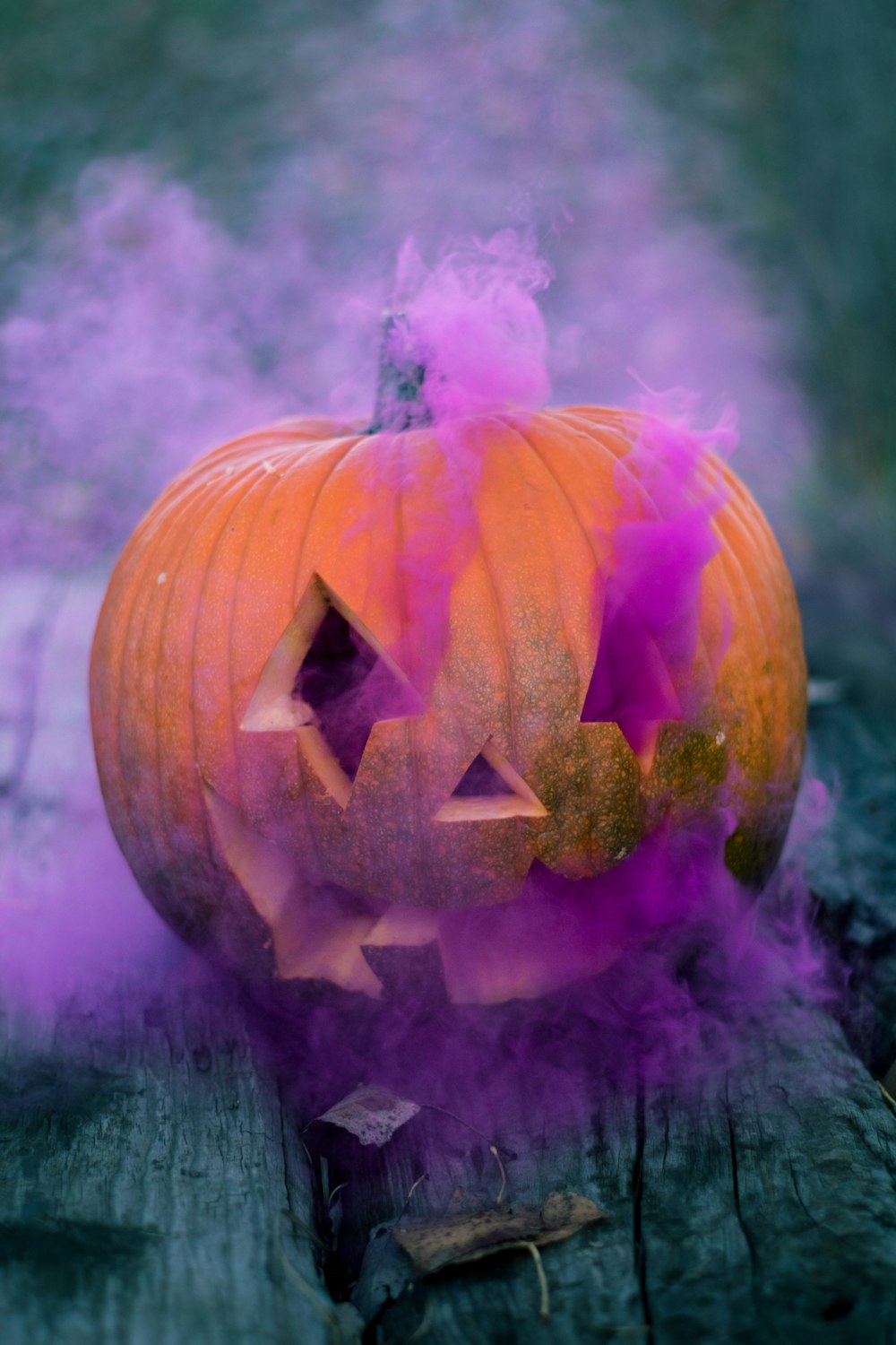 Jack-o'-lantern arancione con fumo rosa su superficie di legno grigio