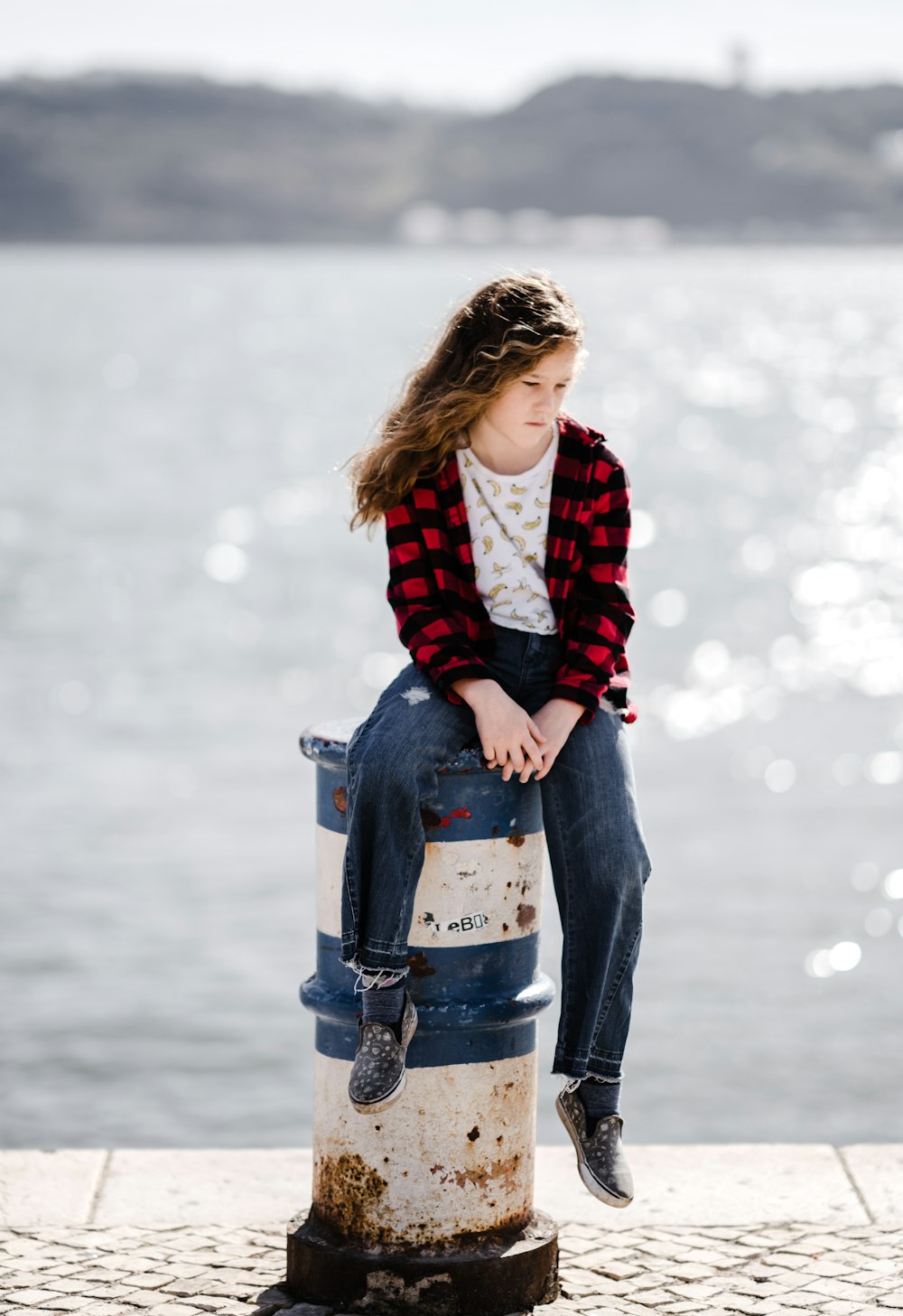 Femme en chemise noire et rouge assise sur une borne au port